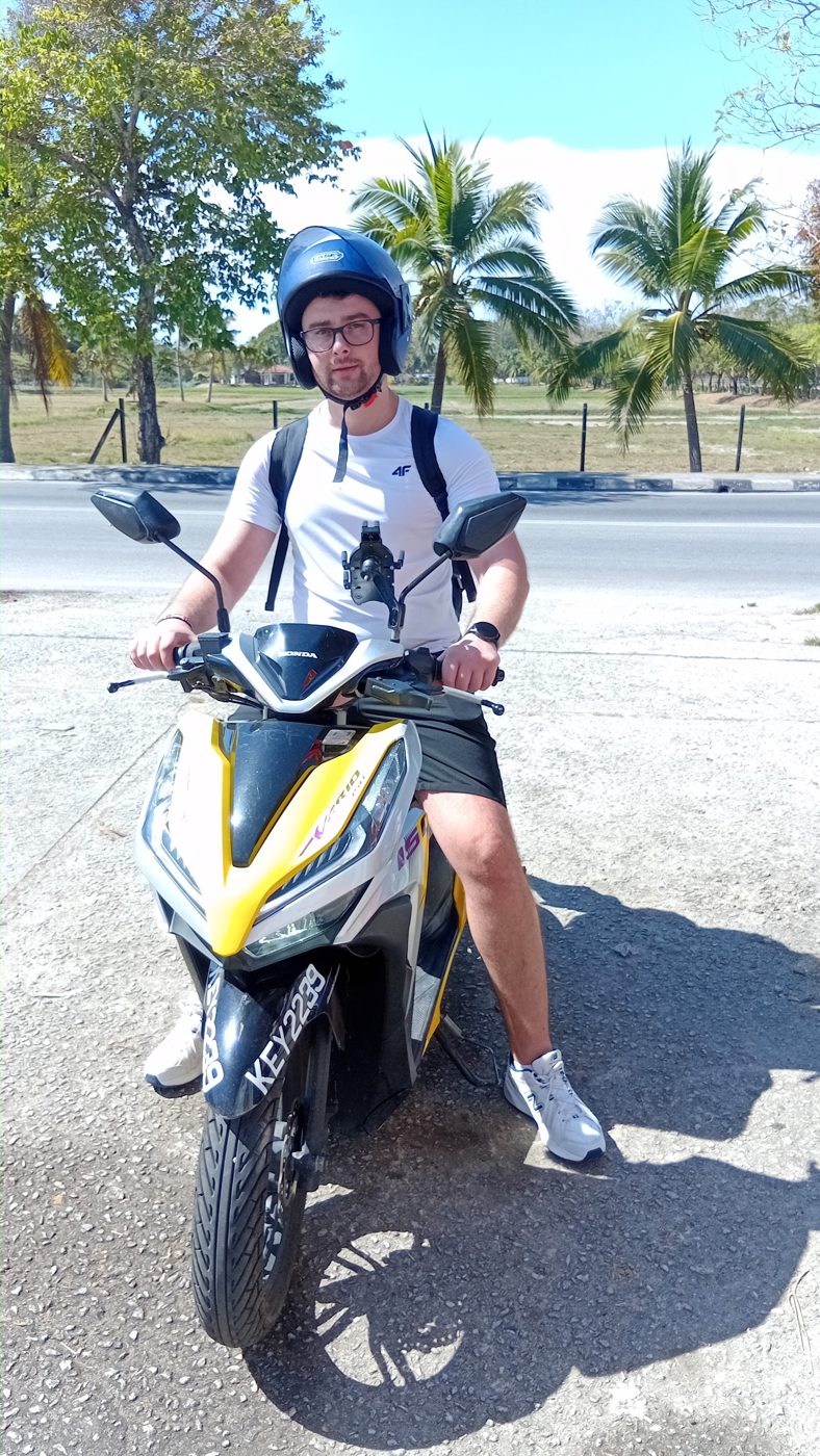 Rider on a white and yellow scooter by palm trees